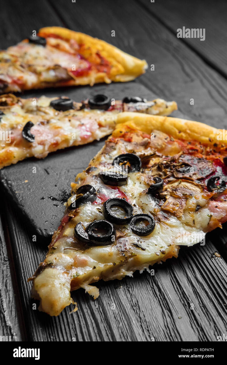 Des morceaux de pizza sur planche de bois noir foncé, des pizzas italiennes traditionnelles Banque D'Images