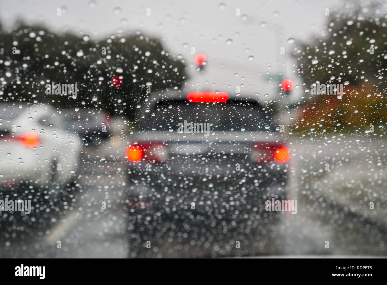 Gouttes de pluie sur le pare-brise un jour de pluie ; voitures arrêtées à un feu rouge à l'arrière-plan ; Californie Banque D'Images