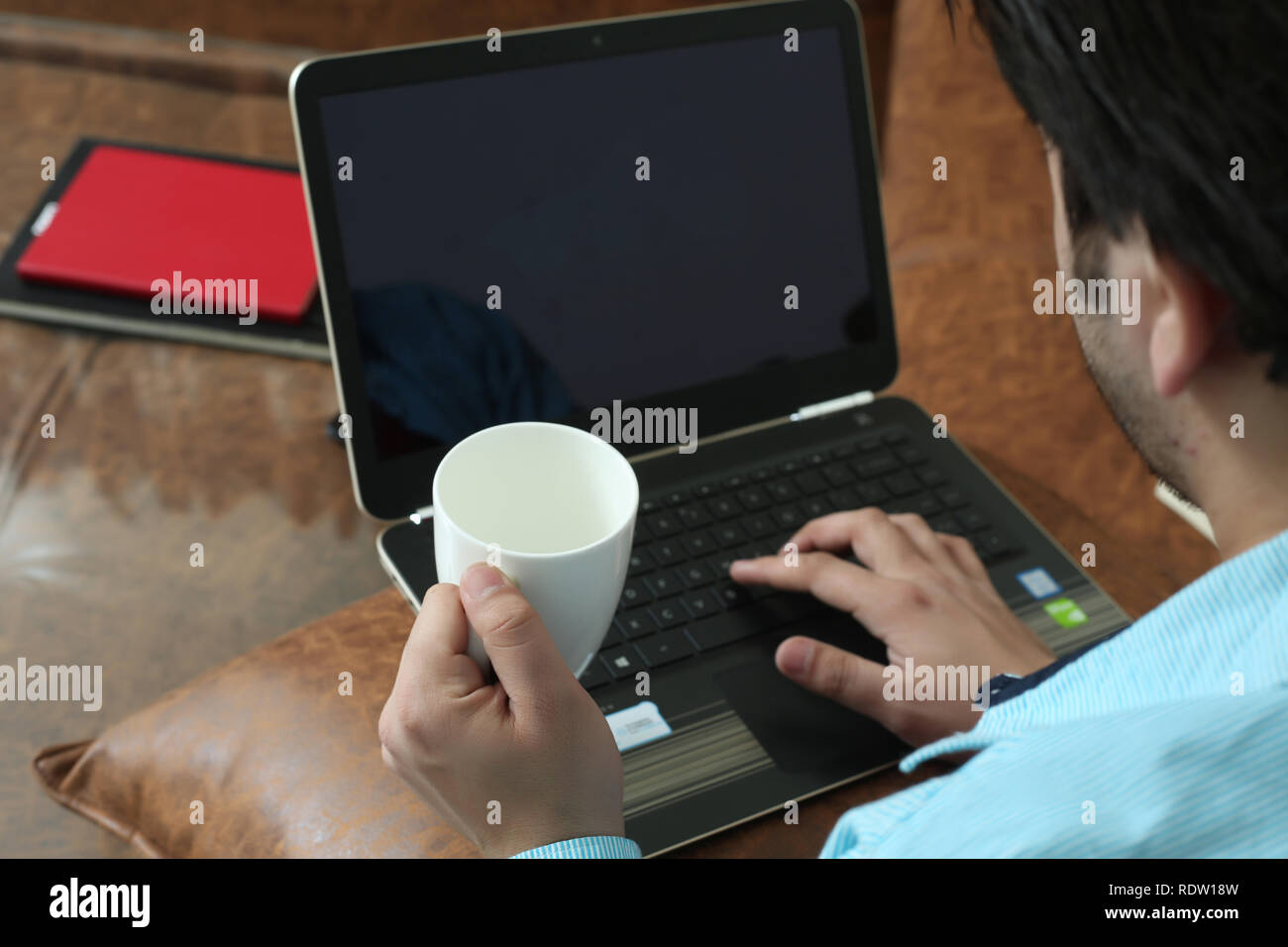 L'homme est à l'aide d'un ordinateur portable avec holding cup dans la main. Banque D'Images
