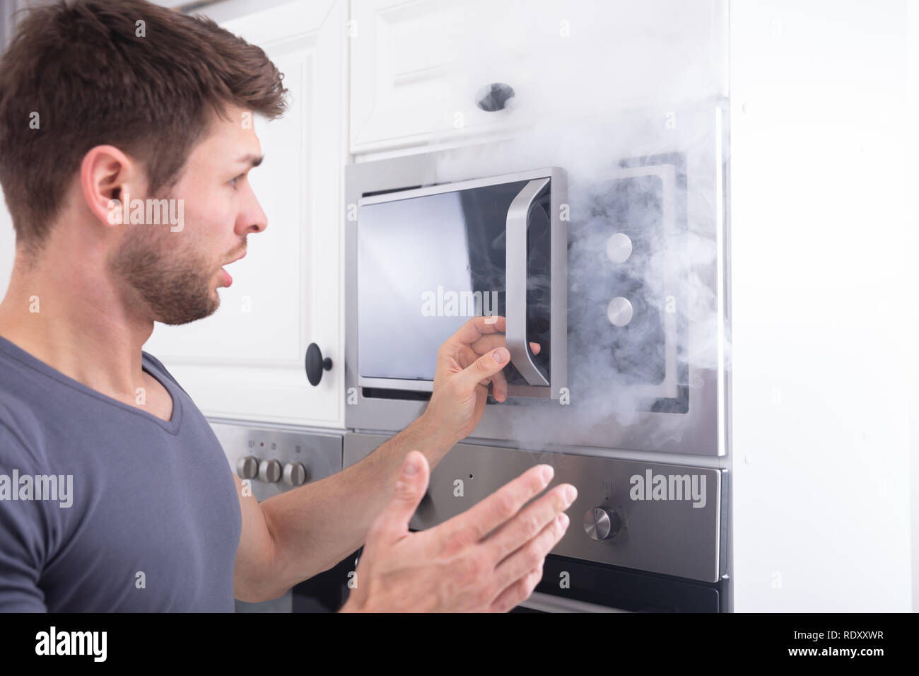 Jeune homme choqué en regardant la fumée s'échapper de four dans la cuisine Banque D'Images