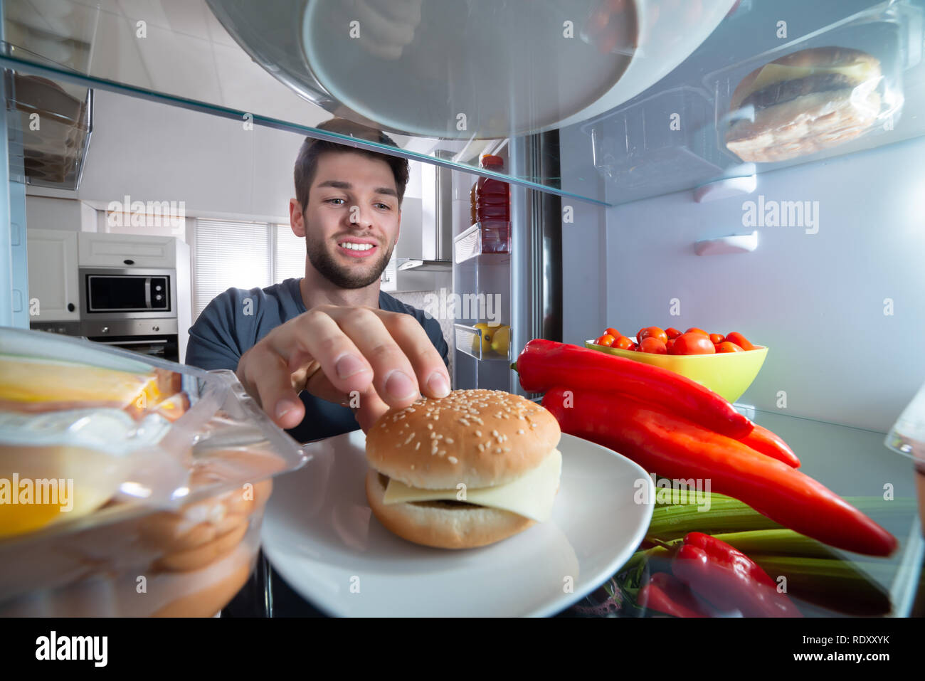 Smiling Young Man Burger dans réfrigérateur Banque D'Images