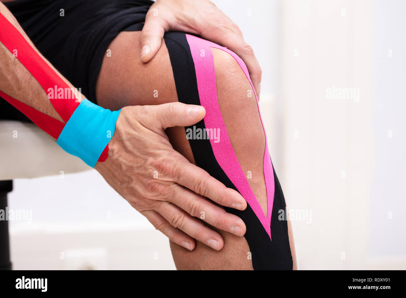 Homme assis sur la table l'application de la kinésiologie tape sur son genou Banque D'Images