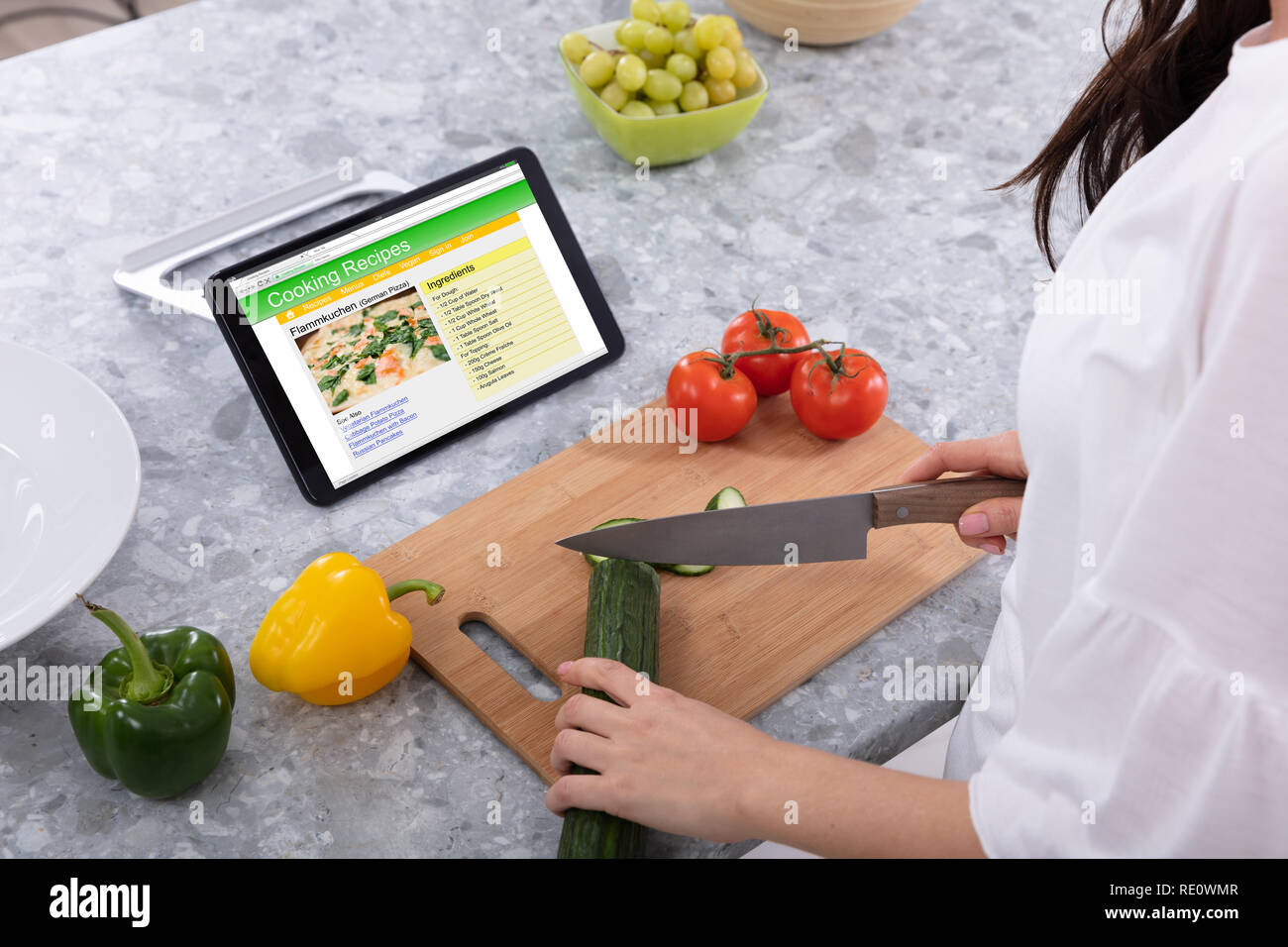 Coupe femme Concombre avec couteau de cuisine près de recettes de cuisine sur écran de tablette numérique Banque D'Images