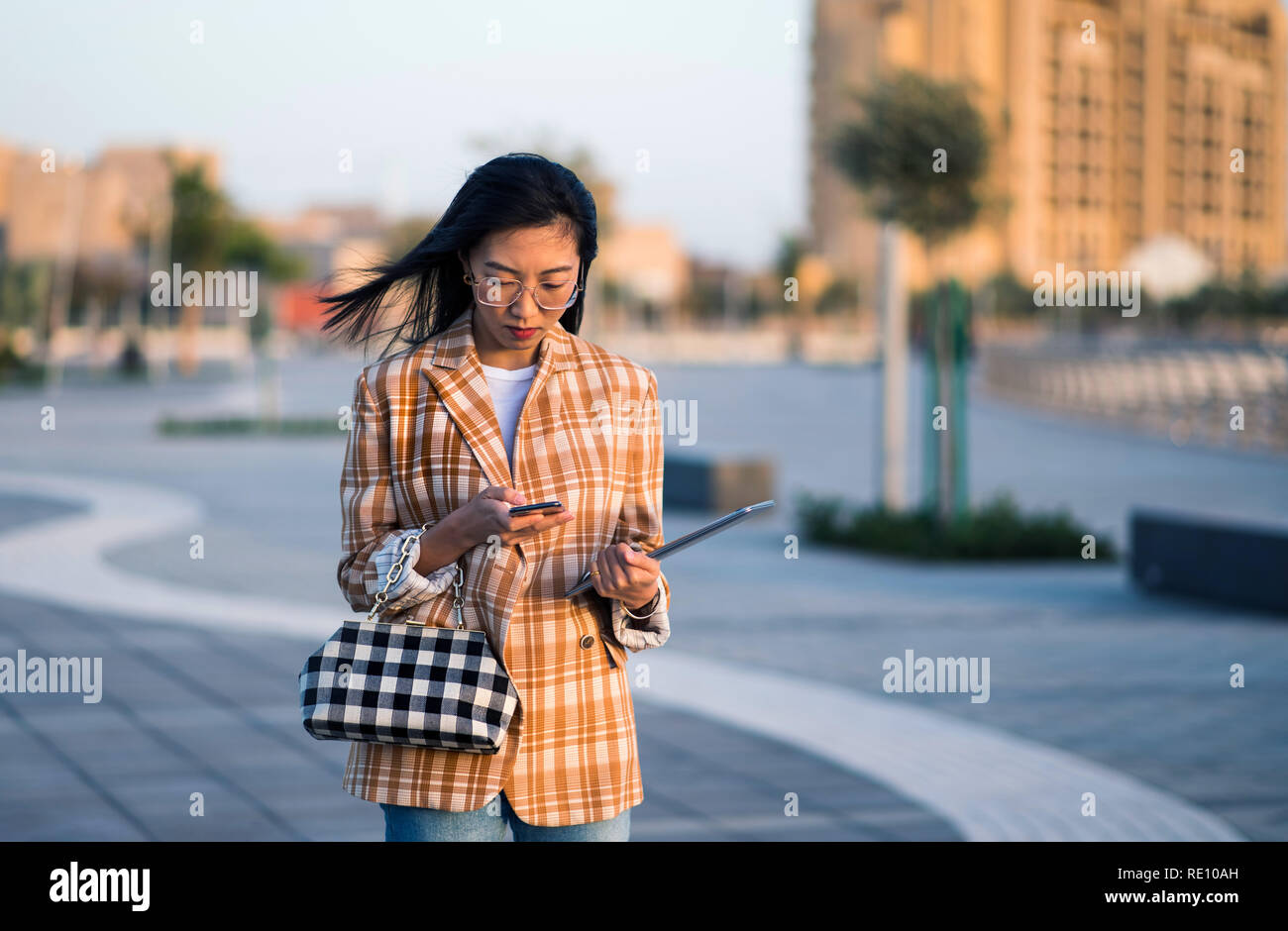 Fille à la mode à l'aide de téléphone et la marche à l'extérieur Banque D'Images