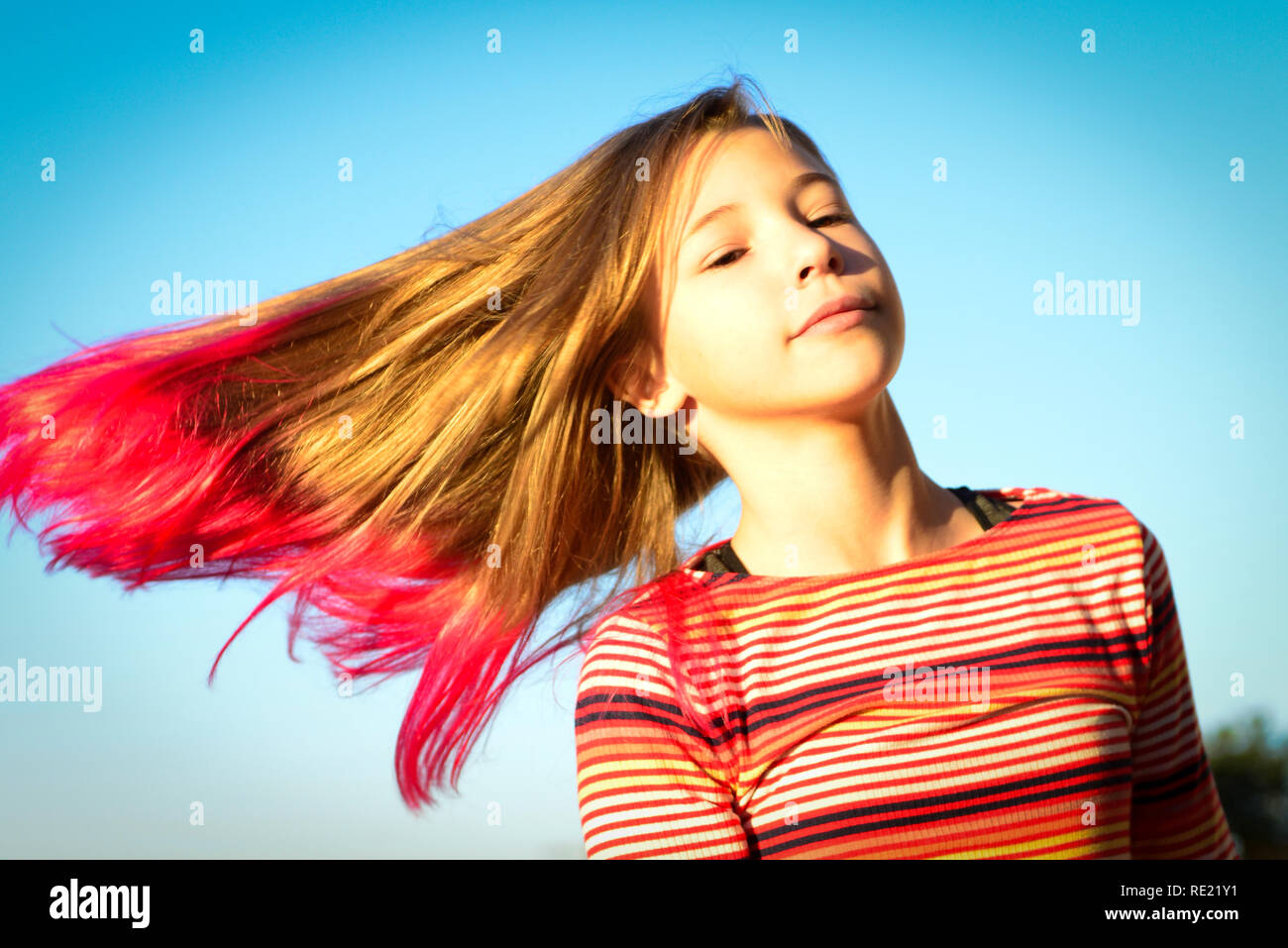 Le Tween girl est isolé contre le ciel tout en faisant tournoyer et balançant ses cheveux blonds à pointe rose à la mode Banque D'Images