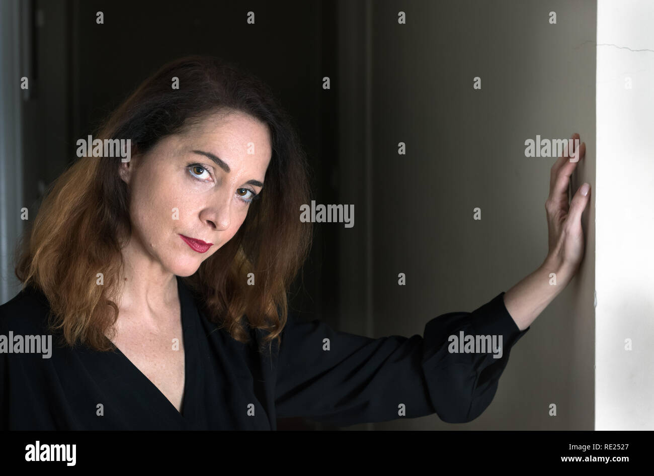 Portrait d'une femme de 48 ans, à la grave, pensive avec sa main sur un mur. Banque D'Images