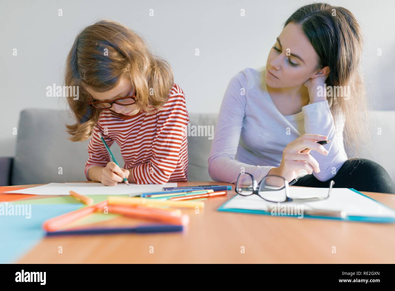 Jeune femme professeur donnerait des cours particuliers à l'enfant, petite fille assise à son bureau écrivant en ordinateur portable. Banque D'Images