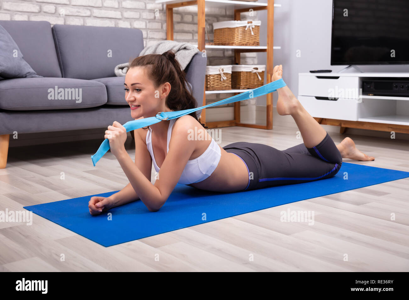 Happy Young Woman in Sportswear faisant d'entraînement par courroie de Yoga à la maison Banque D'Images