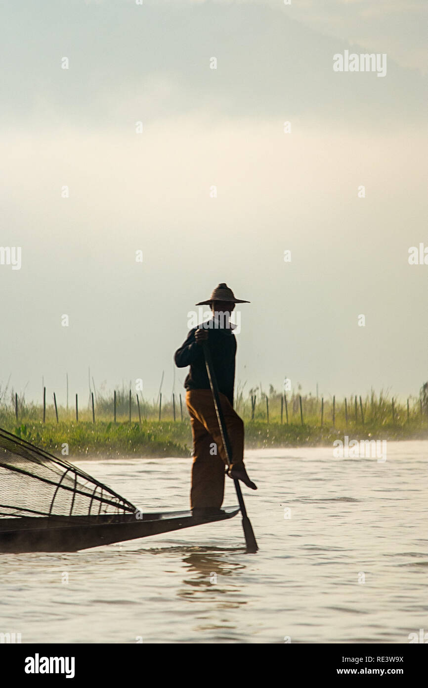 Pêcheur d'ethnie Intha au Lac Inle, à la pêche dans leur style traditionnel dans la lumière du matin. Banque D'Images