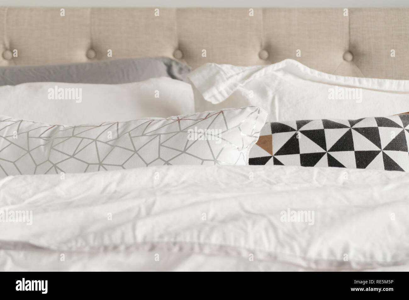 La literie oreillers décoratifs en gris, blanc, noir, or et blanc de la literie. Tête de lit en tissu beige à l'arrière-plan. Lit confortable et moelleux à la Banque D'Images