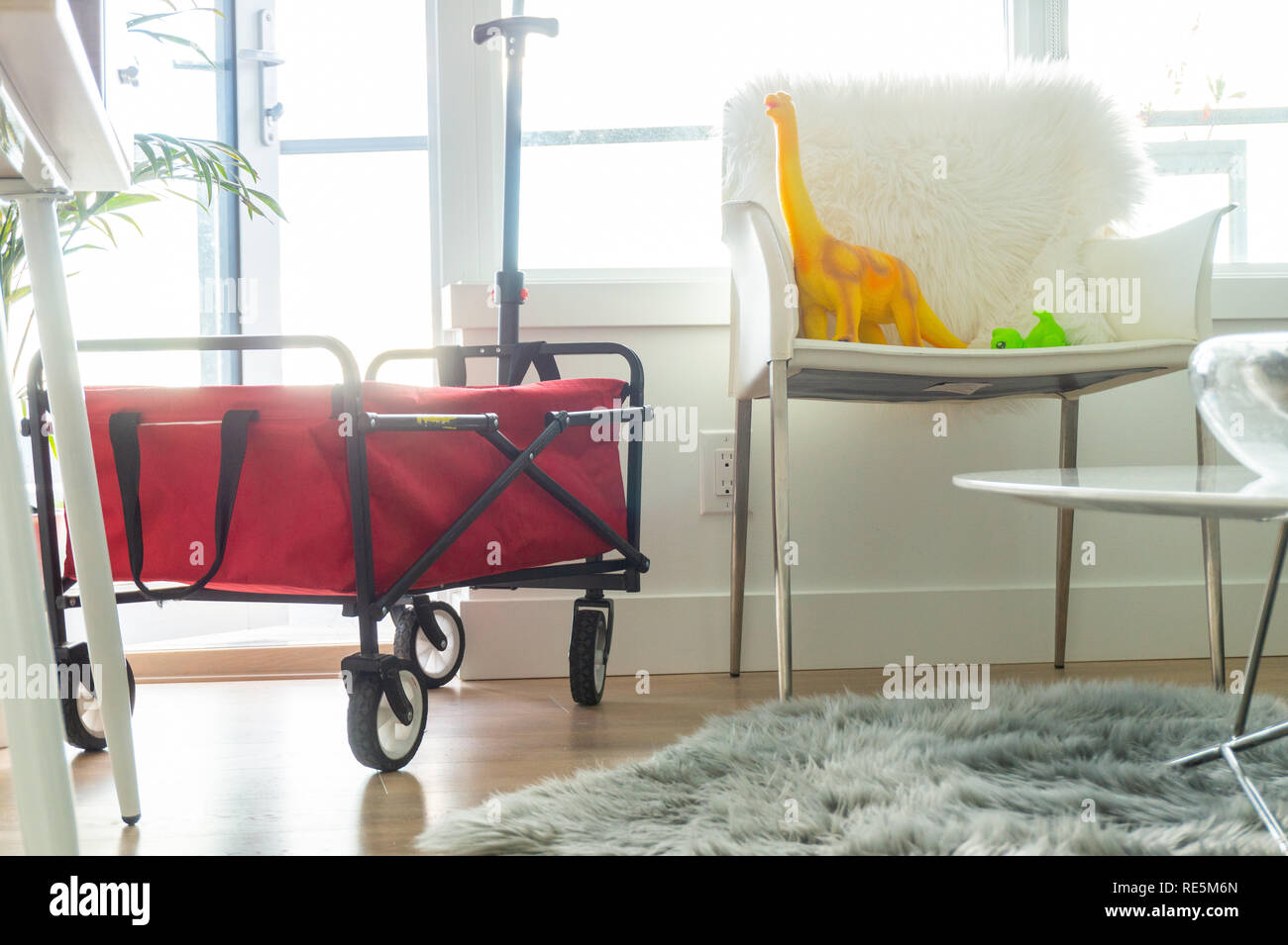 Chariot pliable rouge dans cet appartement lumineux salon, avec jouets dinosaure assis sur une chaise. La fausse fourrure gris tapis sur le plancher. Banque D'Images