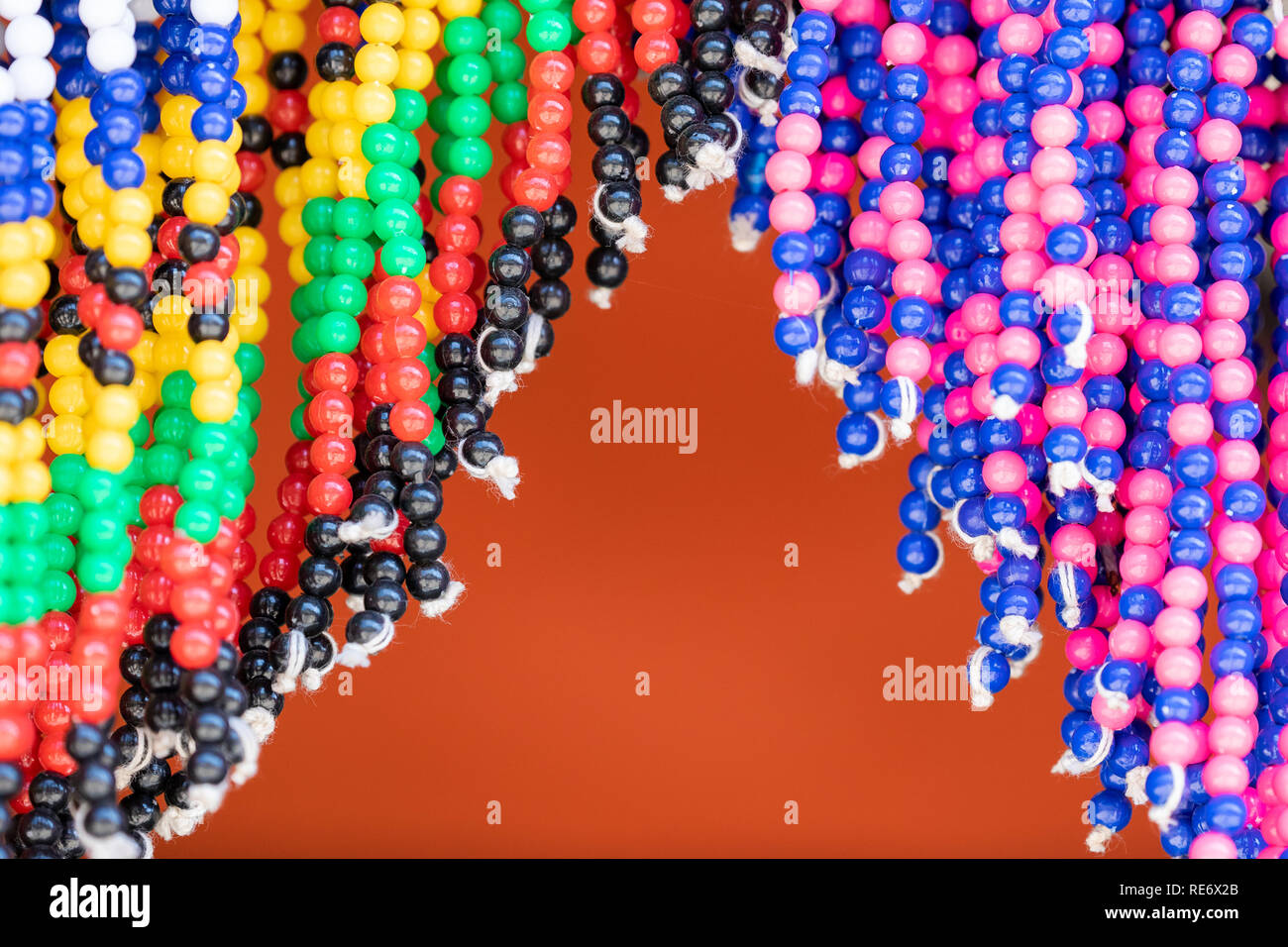 Détail de costume de perles traditionnelles à vendre dans un marché en Afrique du Sud. Des chaînes de perles multicolores accrocher contre un fond orange. Banque D'Images