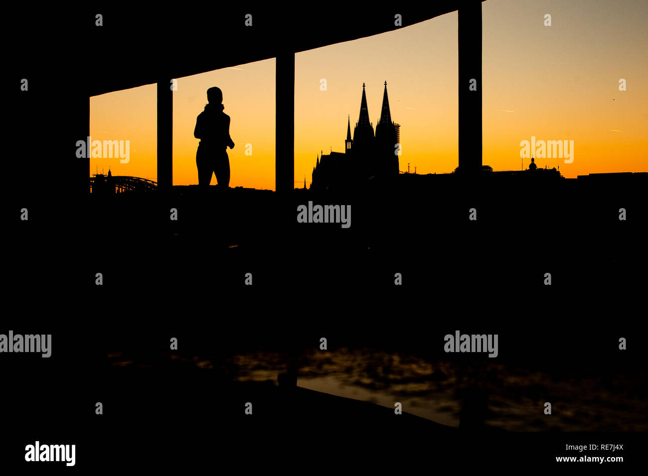 Eine Frau joggt bei Sonnenuntergang durch eine Unterführung am Rhein. Im Hintergrund zeichnet sich der Kölner Dom ab. Banque D'Images