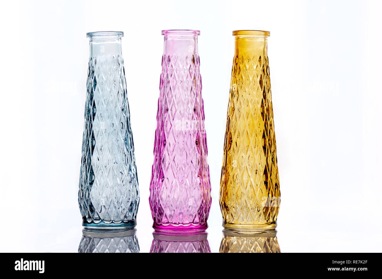 Trois vases de verre coloré avec un motif, isolé sur un fond clair avec la réflexion. Banque D'Images