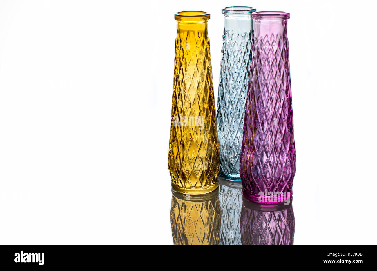 Trois vases de verre coloré avec un motif, isolé sur un fond clair avec la réflexion. Banque D'Images