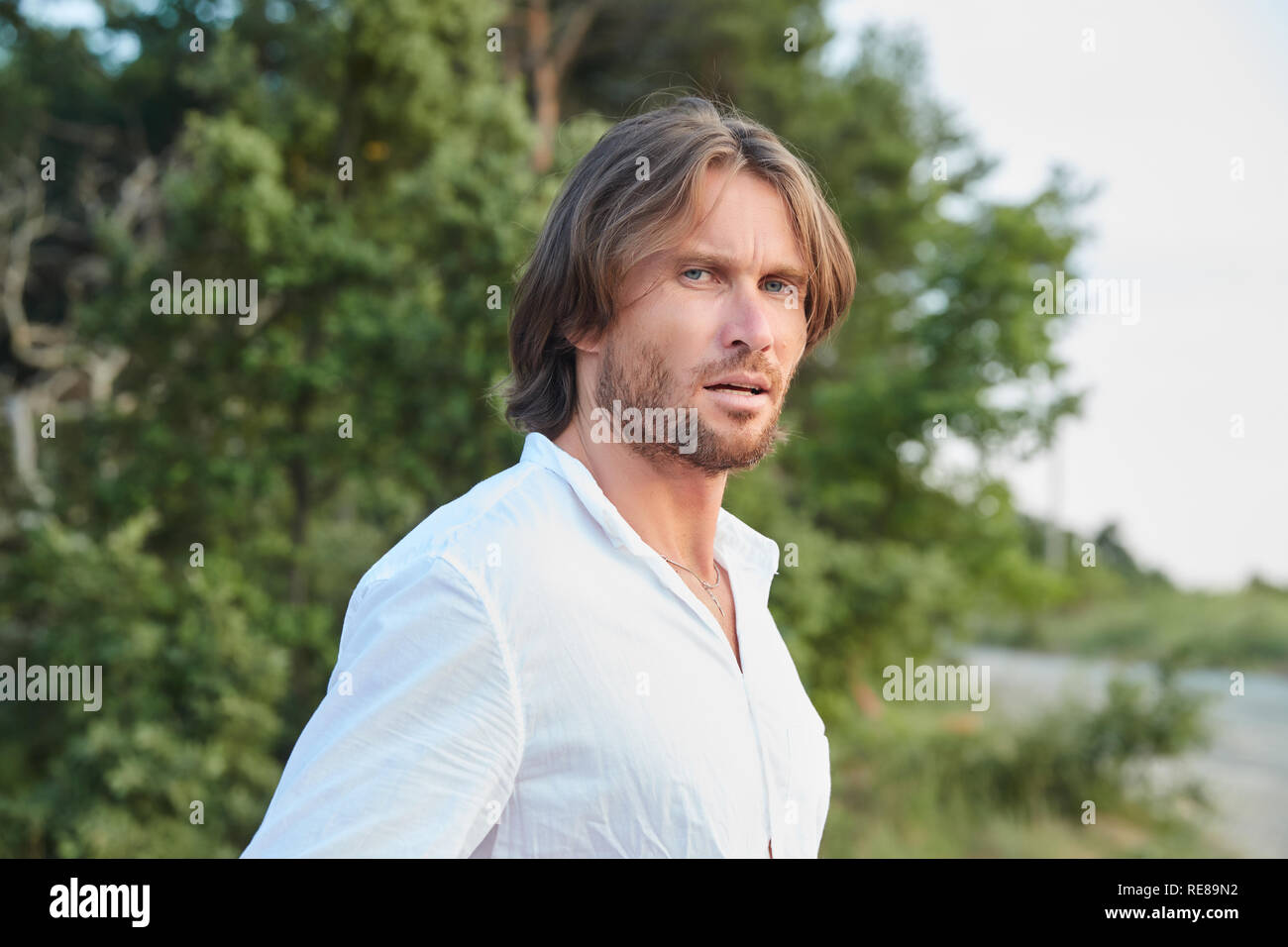 Portrait du jeune homme brutal beau avec les cheveux longs, les yeux bleus, un moyen facile de soies, il est habillé d'une chemise blanche avec un manche courte Banque D'Images