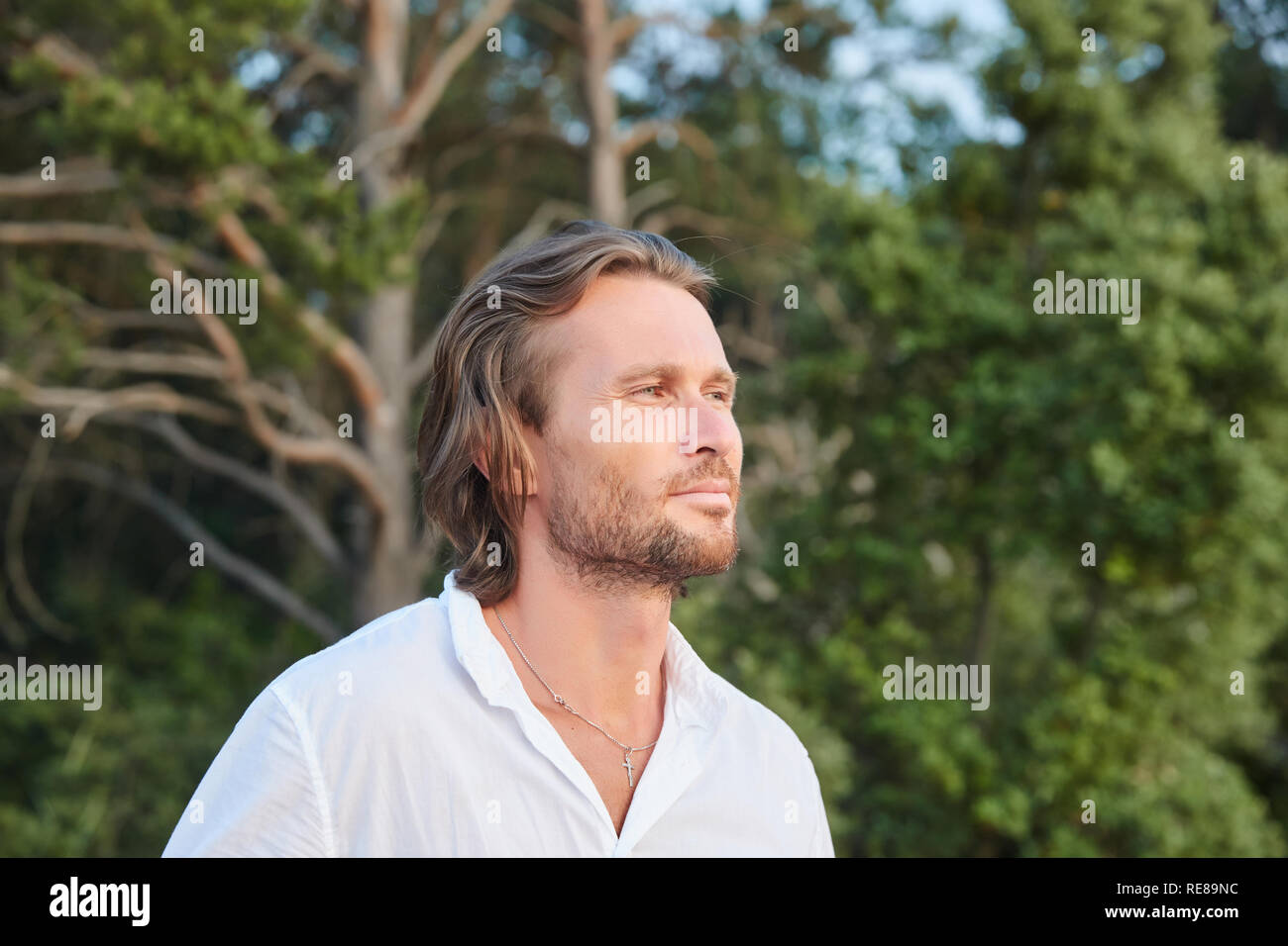 Portrait du jeune homme brutal beau avec les cheveux longs, les yeux bleus, un moyen facile de soies, il est habillé d'une chemise blanche avec un manche courte Banque D'Images