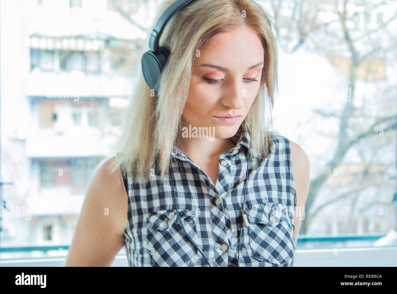 Jeune fille hipster en chemise à carreaux avec un casque à l'écoute de la musique à la maison, arrière-plan flou, concept musique Banque D'Images