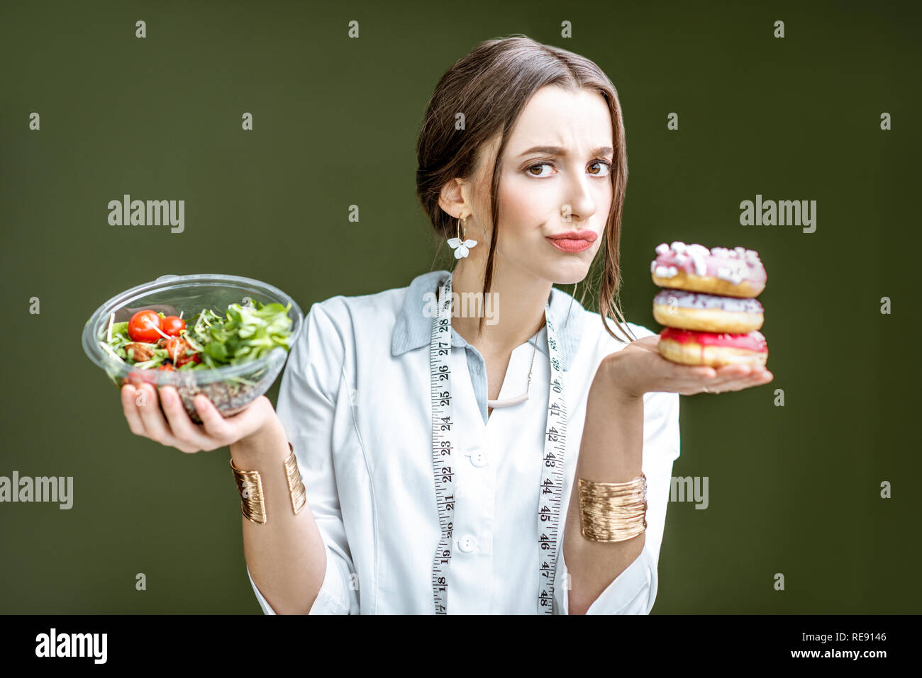 Jeune femme nutritionniste à sur le donuts avec émotions triste de choisir entre la salade et dessert malsaine sur le fond vert Banque D'Images