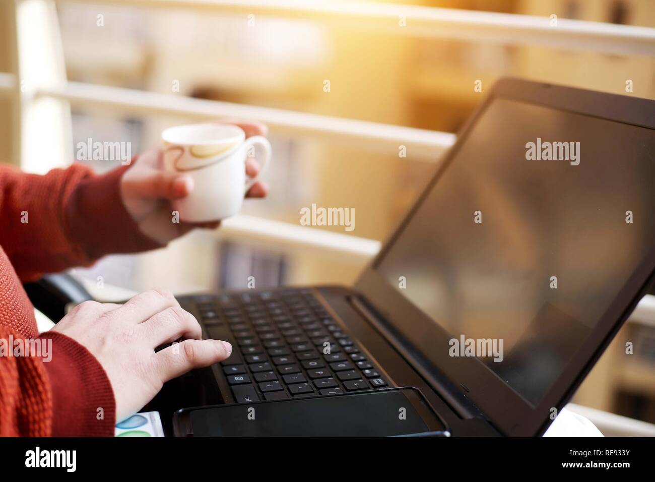 Boy est de travailler sur l'ordinateur portable avec holding cup dans la main. Banque D'Images