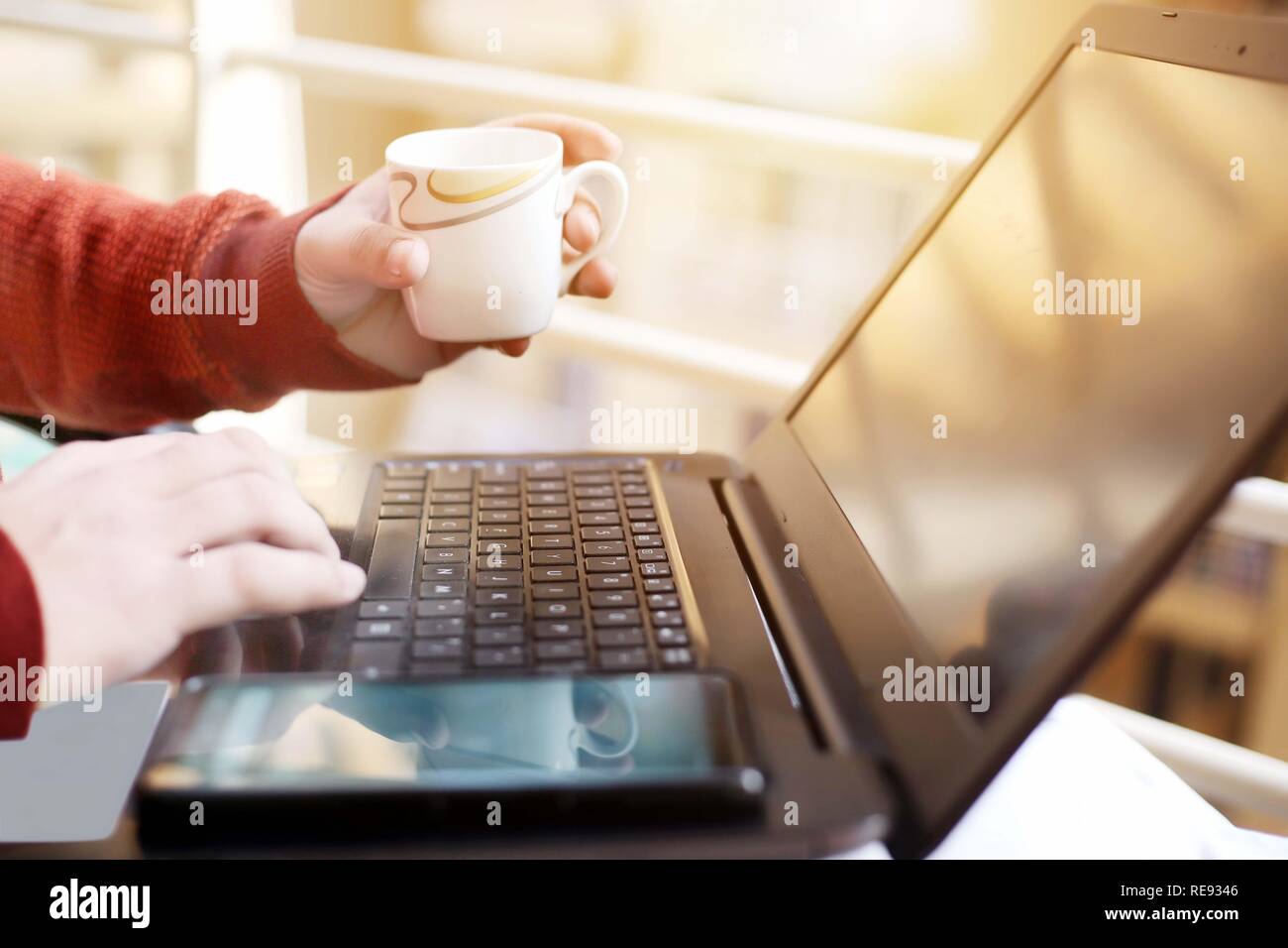 L'homme est de travailler sur l'ordinateur portable avec holding tasse de thé à la main. Banque D'Images