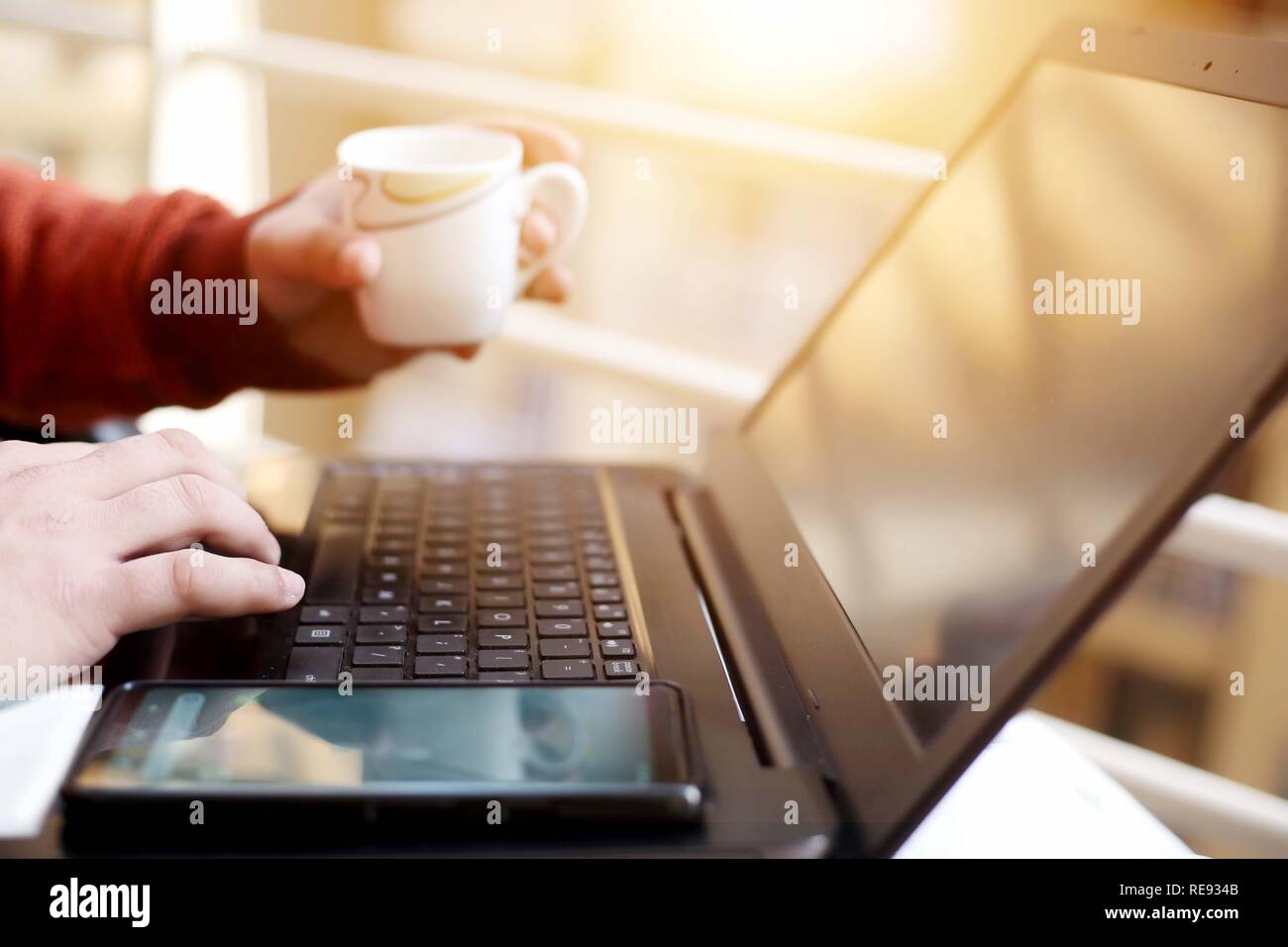 Jeune homme travaille dans l'ordinateur portable avec holding tasse de thé à la main. Banque D'Images