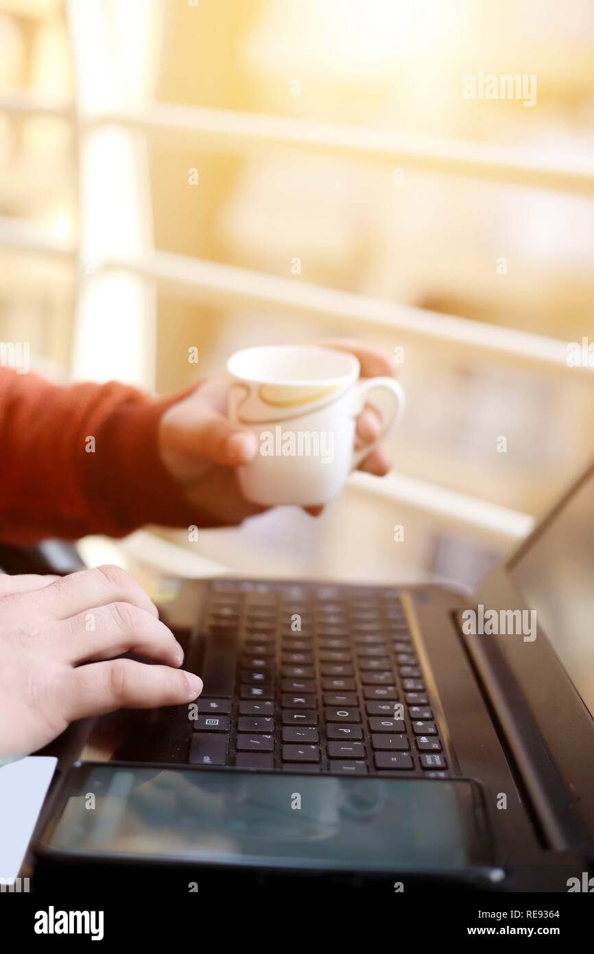 L'homme est à l'aide d'un ordinateur portable avec holding tasse de thé à la main. Banque D'Images