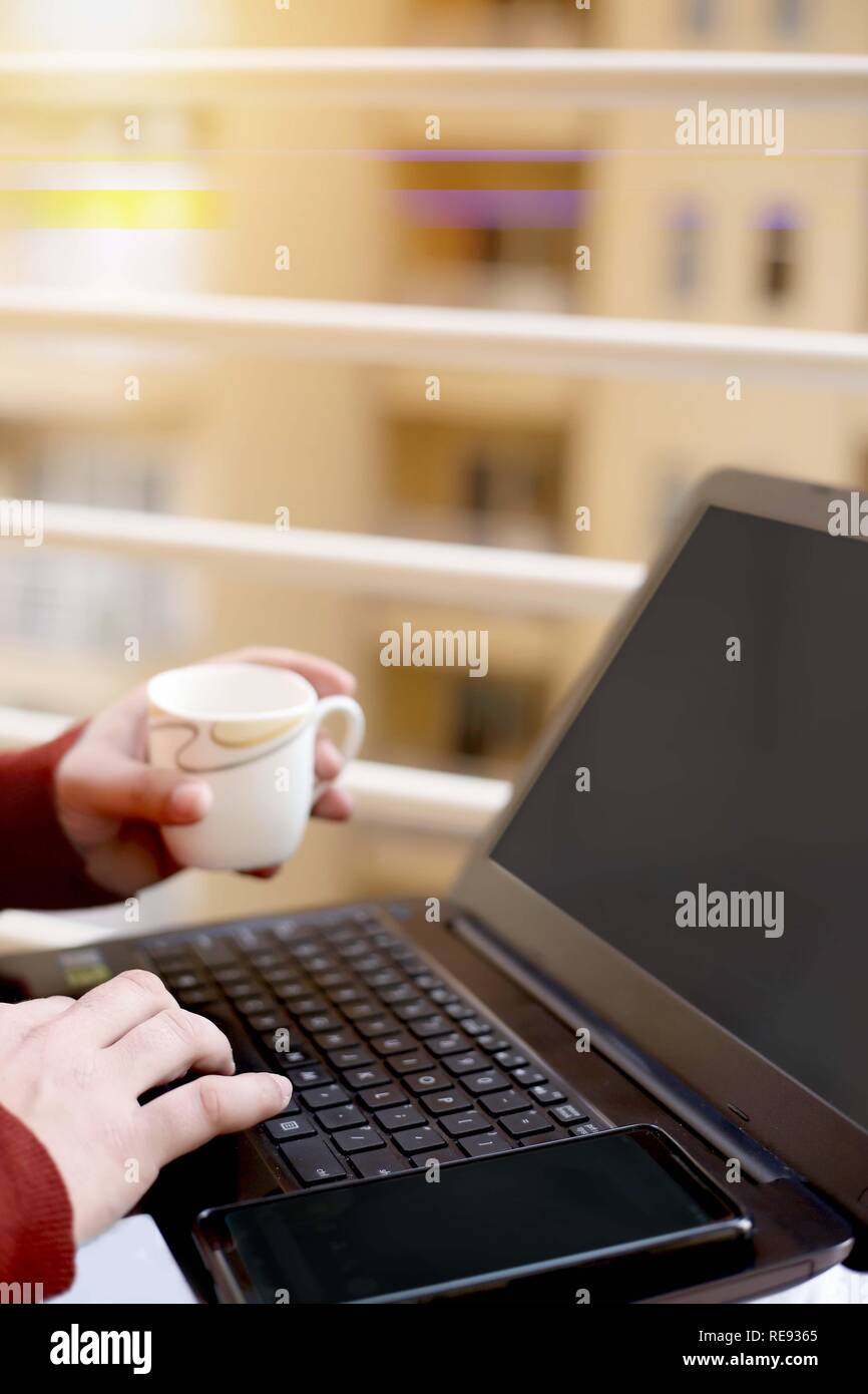 Boy est à l'aide d'un ordinateur portable avec holding cup dans la main. Banque D'Images