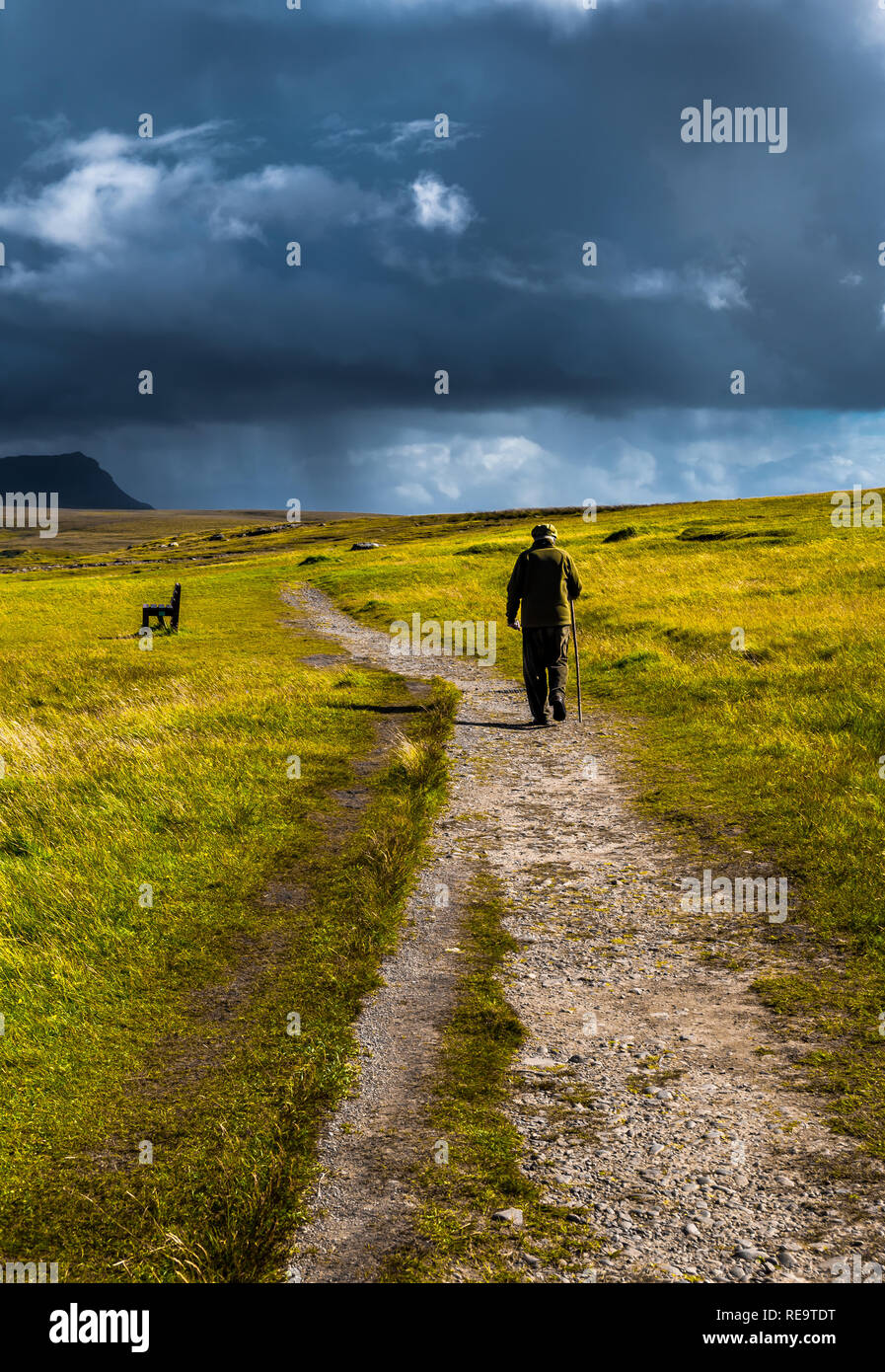 Vieil Homme avec bâton de marche flâne sur le chemin de gravier étroit à travers le paysage pittoresque avec de magnifiques Nuages Banque D'Images