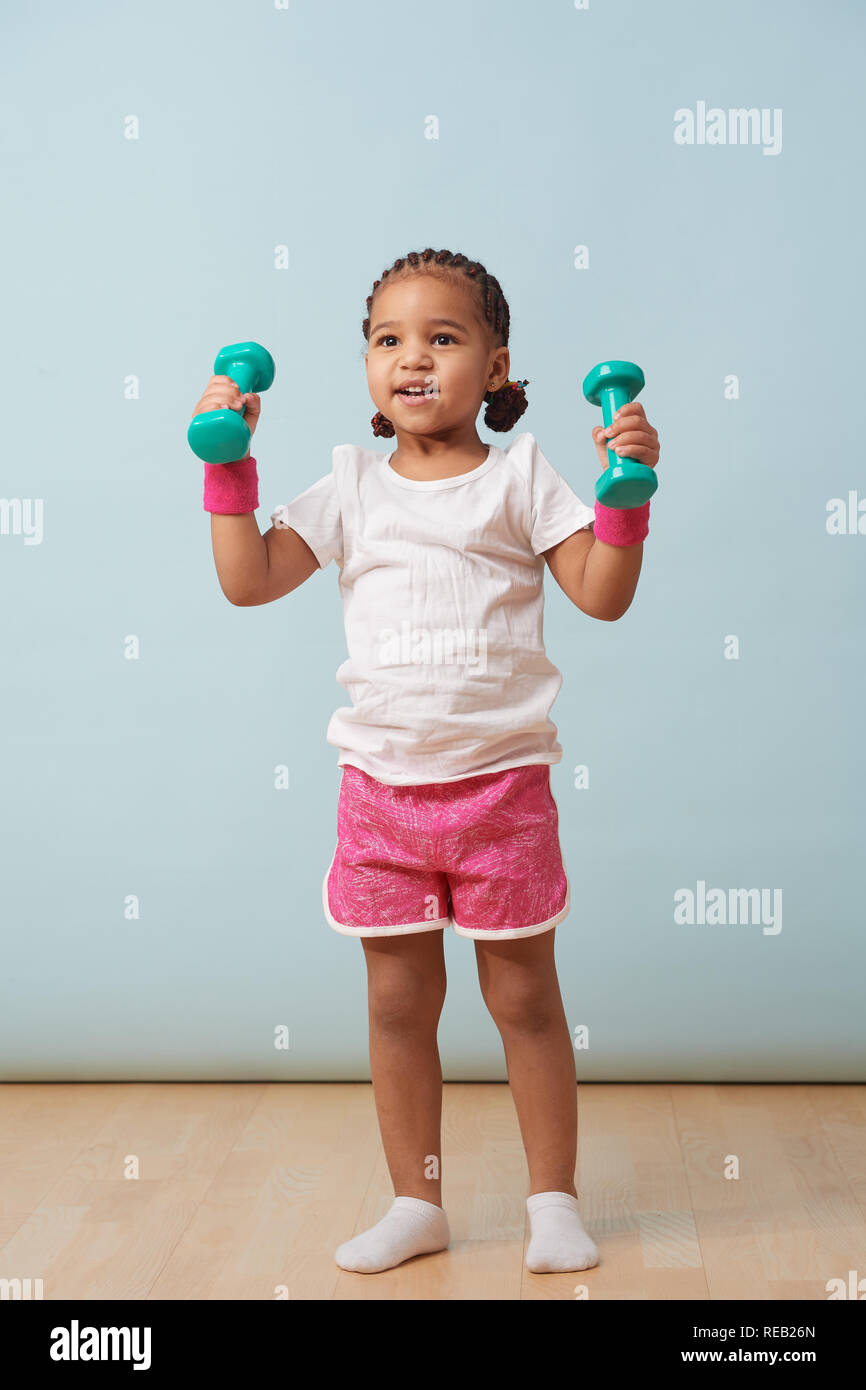 Portrait of cute little girl petite levée haltères de couleur à la maison. Short rose et bracelets. Entraînement de fitness. Banque D'Images