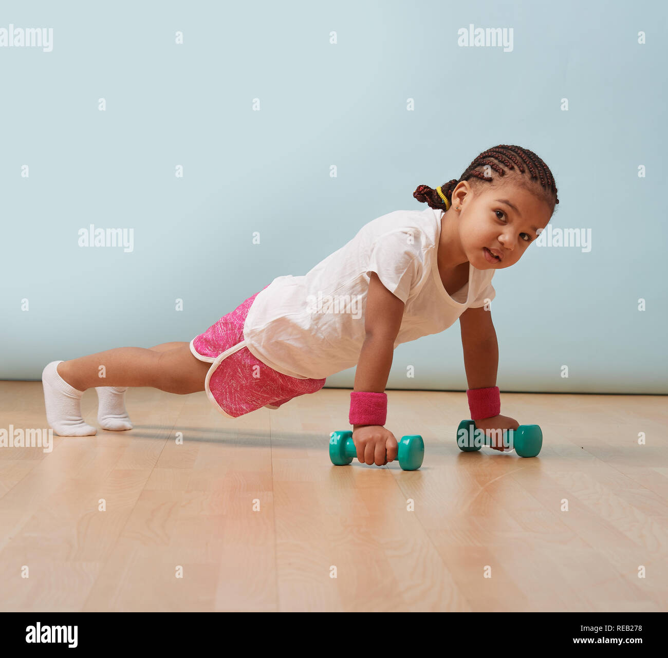 Portrait of cute little girl making poussez se lève sur les haltères à la maison. Short rose et bracelets. Entraînement de fitness. Banque D'Images