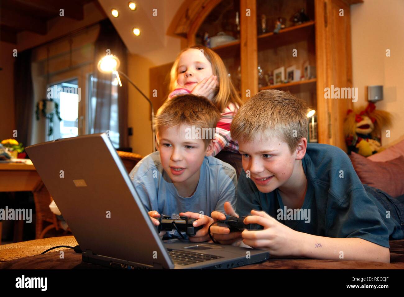 Frères et sœurs, 7, 11, 13 ans, avec un ordinateur portable dans le salon, jouant un jeu d'ordinateur de course de voiture Banque D'Images