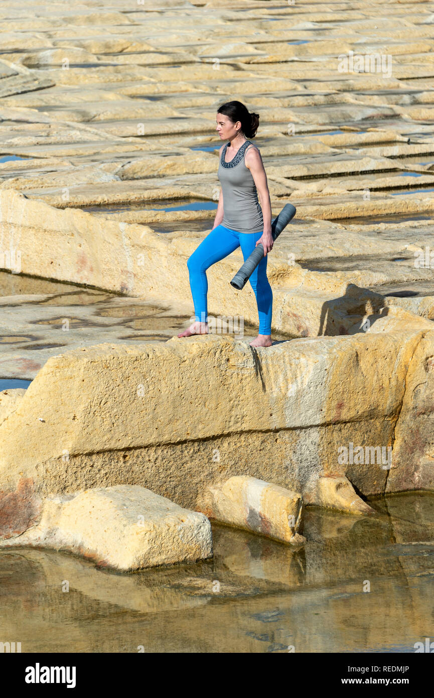 Femme sportive marchant sur les salines de calcaire à Malte transportant un tapis de yoga Banque D'Images