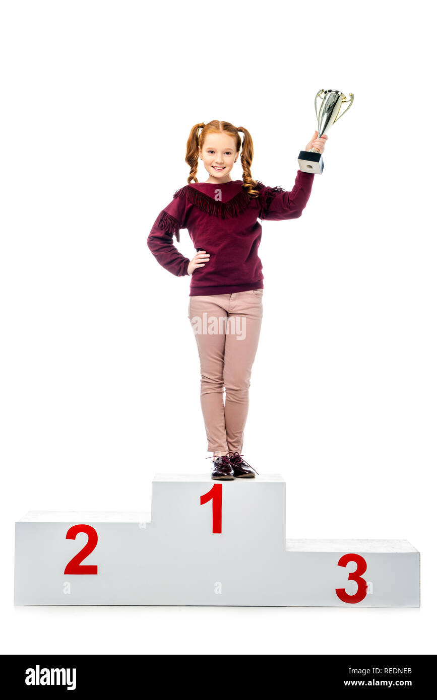 Cheerful lycéenne debout sur le podium gagnant, smiling, holding trophy cup and looking at camera isolated on white Banque D'Images