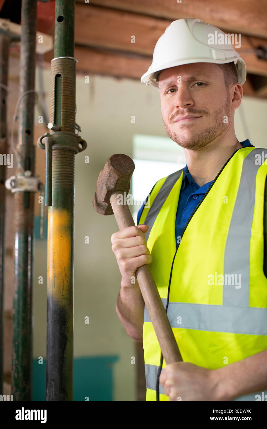 Portrait of Construction Worker With Sledgehammer démolir Mur dans maison rénovée Banque D'Images