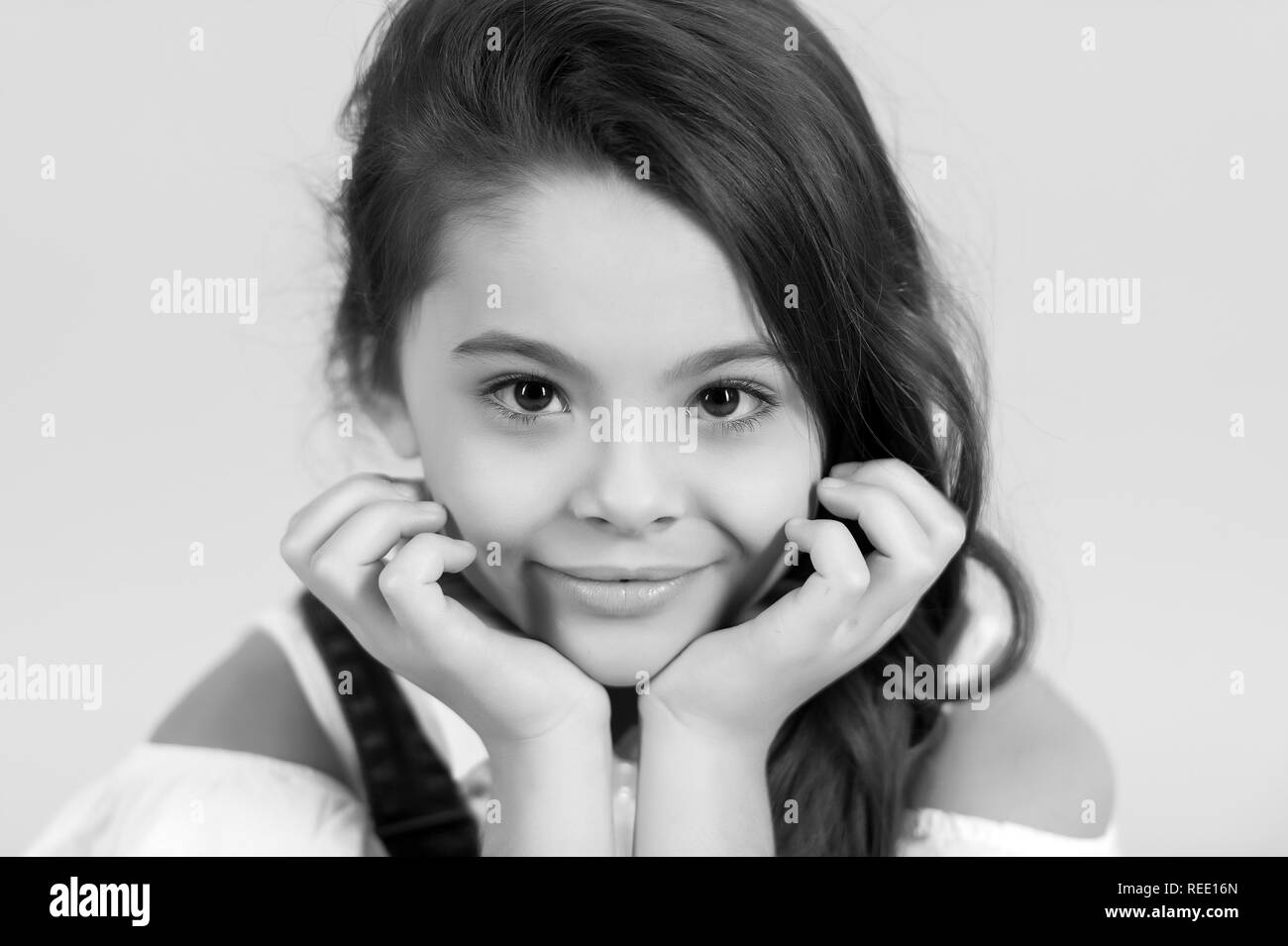 Petite fille avec le sourire adorable visage sur fond bleu. Pose de l'enfant avec les mains au visage peau sains jeunes. La peau, la santé, de la jeunesse. Beauté, look, coiffure, pastel punchy Banque D'Images