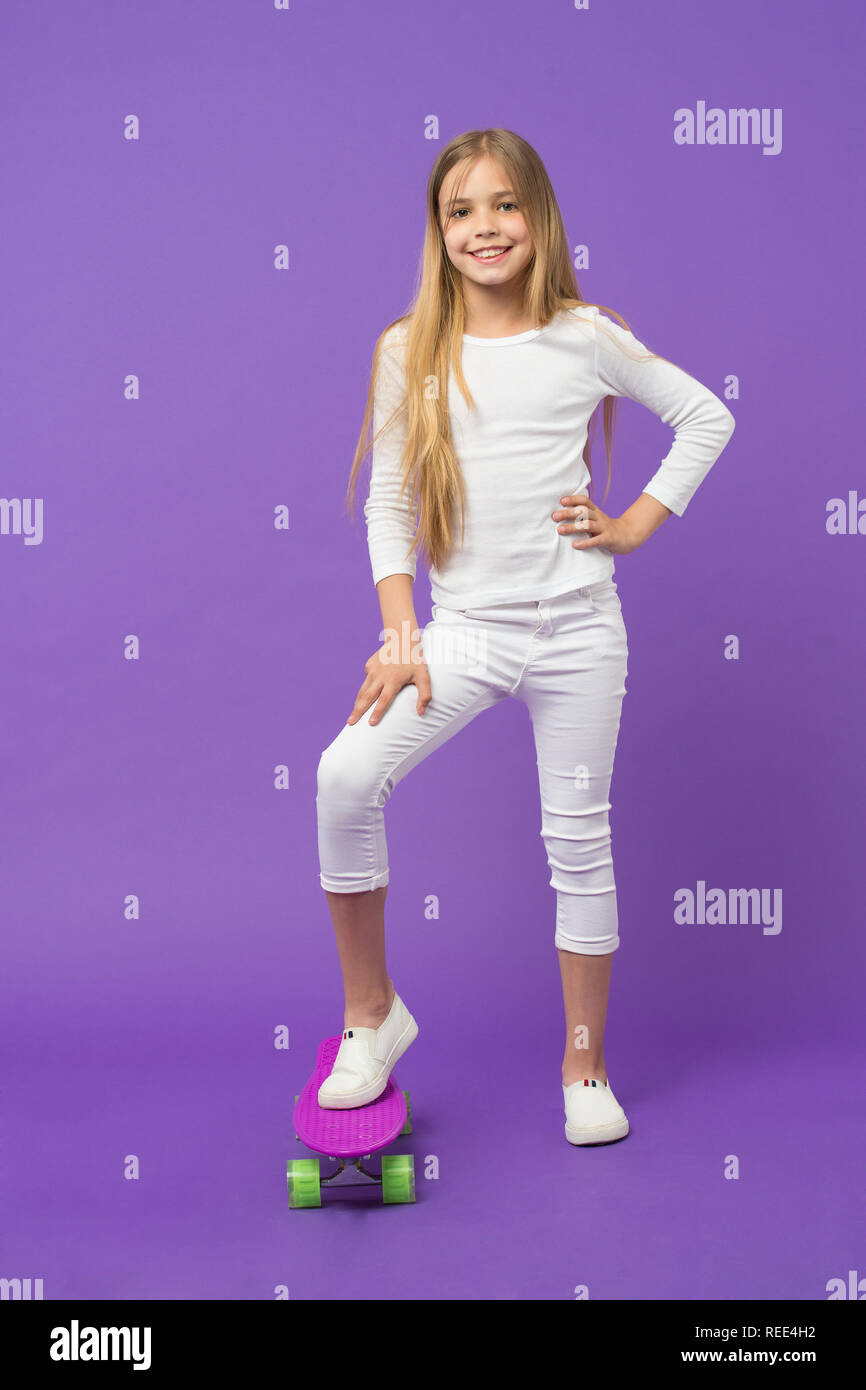 Skateboard kid en vêtements de détente sur fond violet. Skater Girl smiling  with longboard. Petit enfant sourire avec skate board. L'activité sportive  et de l'énergie. Vie de l'enfance et des jeux actifs