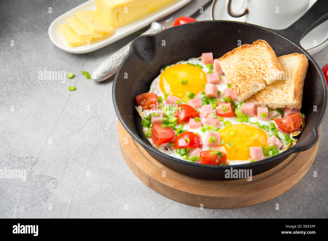 Oeufs frits en noir poêle avec du jambon, tomates cerises et oignons verts de printemps. Délicieux petit déjeuner avec du pain grillé et du beurre. Le classique Anglais Banque D'Images