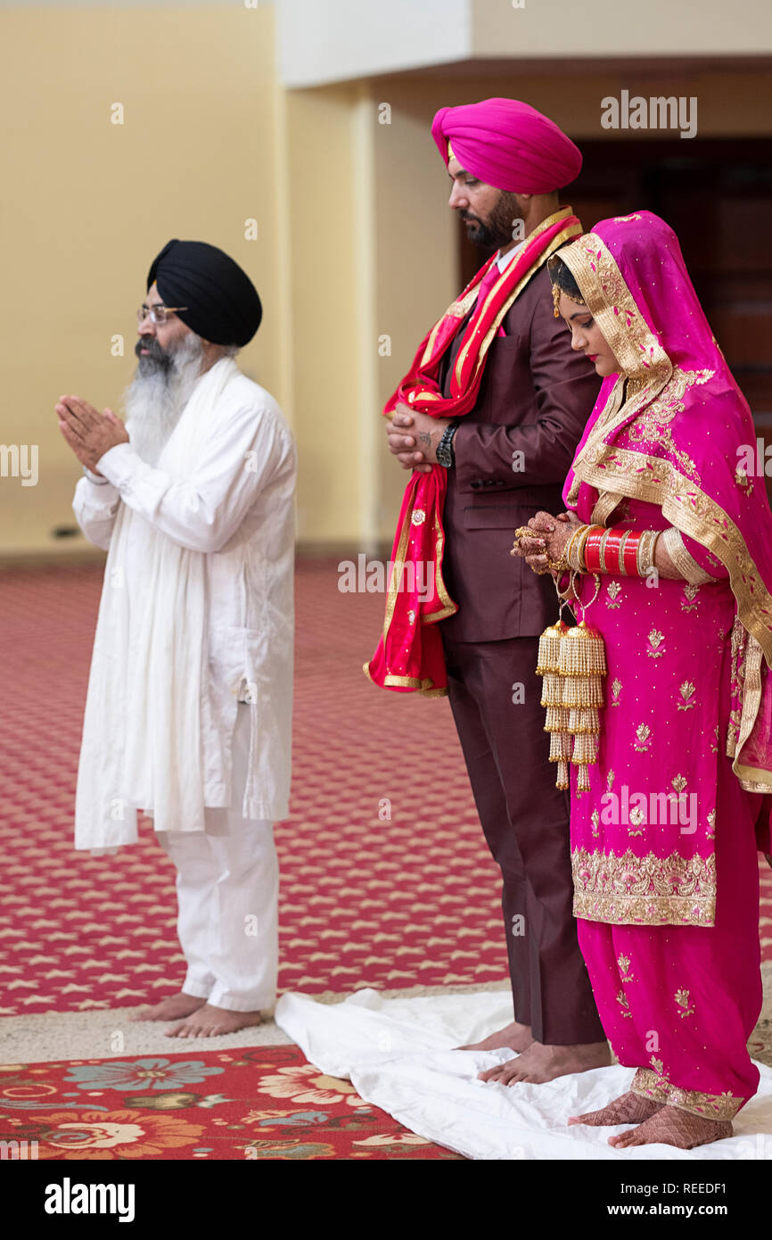 Une épouse pieuse, l'époux et le prêtre qui préside au cours de leur cérémonie de mariage dans un temple sikh à Queens, New York. Banque D'Images