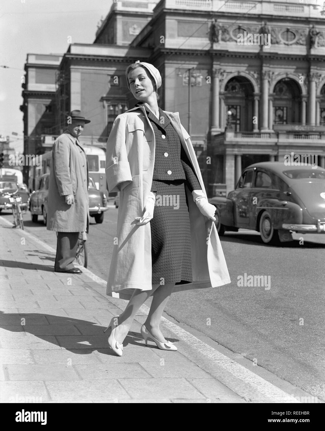 À la mode dans les années 1950. Une jeune femme porte une robe typique des  années 50. Elle pose dans la tenue même si les voitures passe son dans la  rue. La