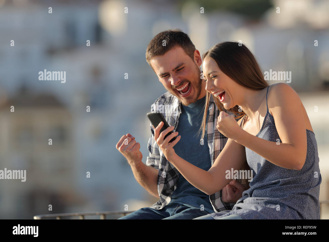 Heureux couple ou amis lire smart phone content dans une ville au coucher du soleil Banque D'Images