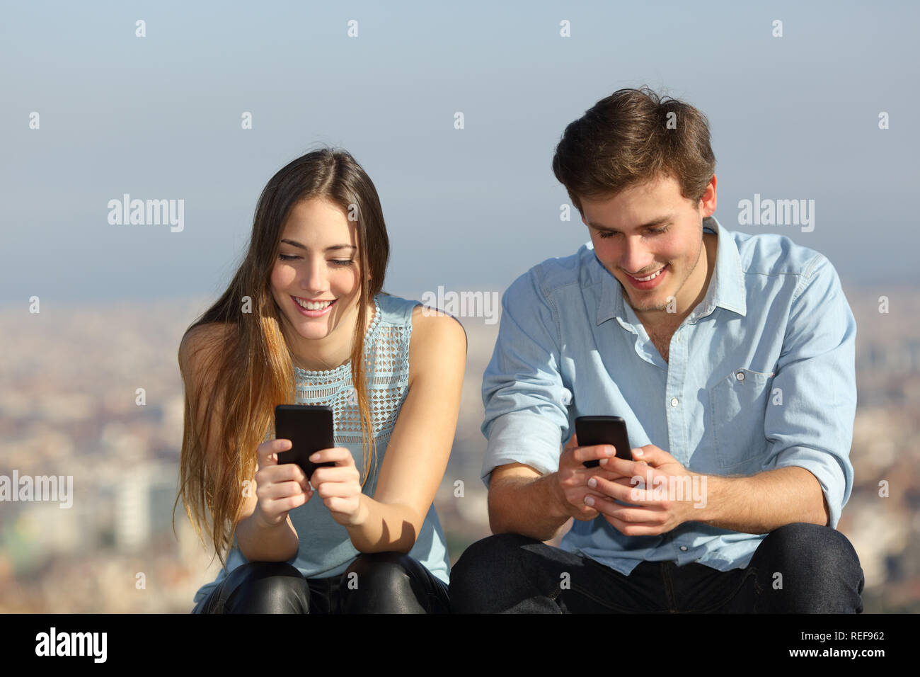 Vue avant portrait d'un couple heureux en utilisant leur téléphone intelligent à l'extérieur dans une ville périphérie Banque D'Images