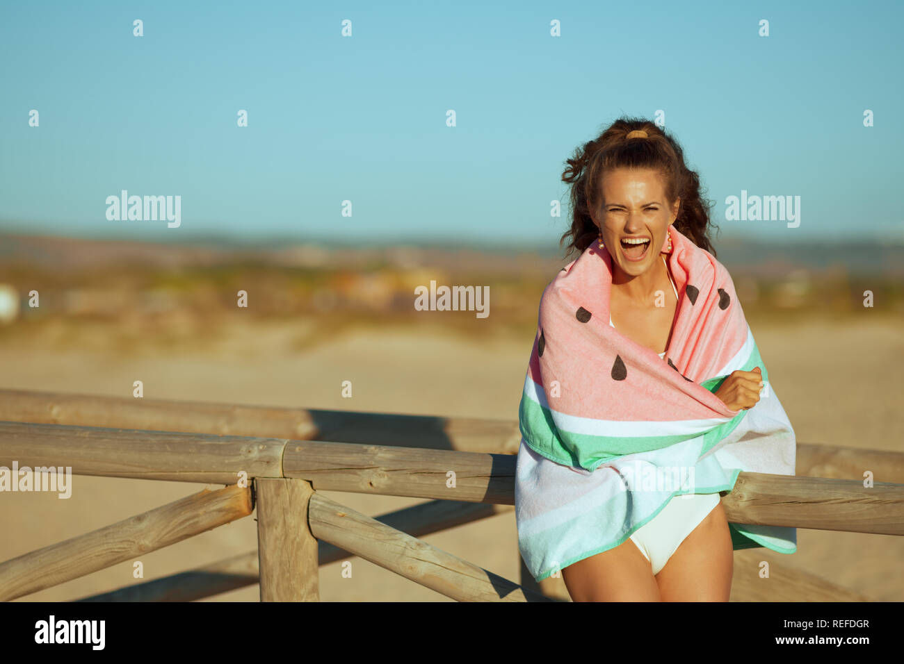 Jeune femme en maillots sur la côte de l'océan dans la soirée, enveloppé dans une serviette pastèque. femme brunette 30 ans quelque chose de standin Banque D'Images