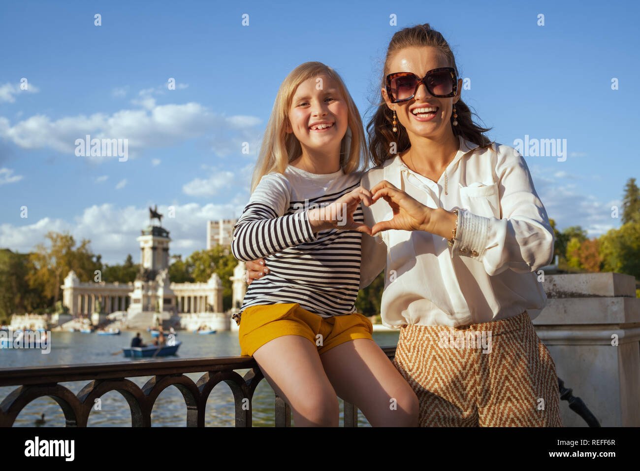 Heureux jeune mère et fille les voyageurs au parc du Retiro à Madrid, Espagne montrant les mains en forme de coeur. l'enfant aux cheveux blonds en t-shirt à rayures et vous Banque D'Images