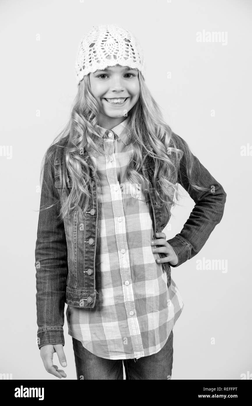 Enfance heureuse concept. Sourire de l'enfant avec de longs cheveux blonds. Beauté, look, coiffure. Fille en costume jeans chemise à carreaux, un chapeau sur fond orange. Fashion style tendance. Banque D'Images