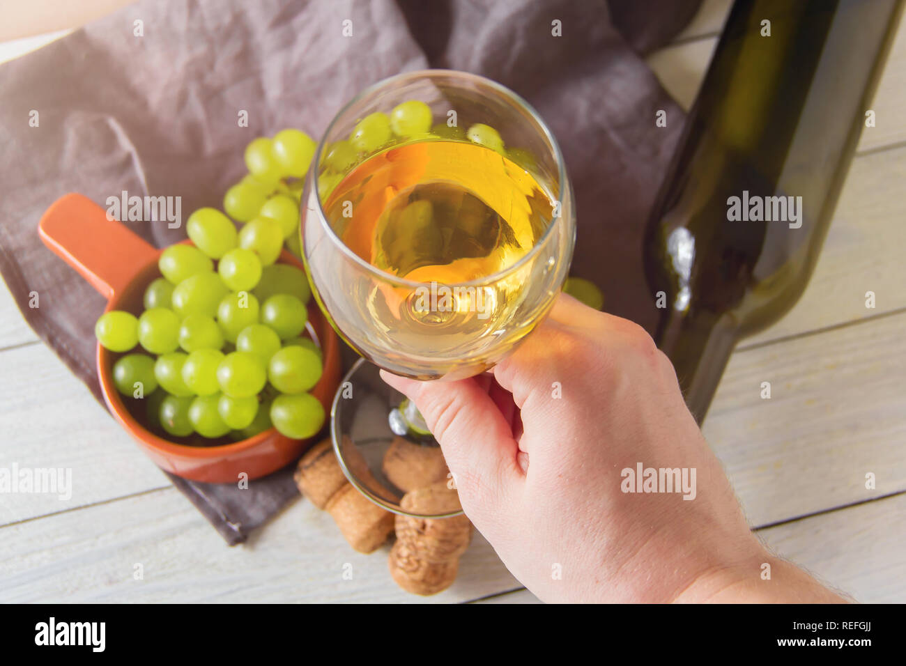 Tenir la main masculine verre de vin contre le verre, bouteilles, bouchons, raisins Banque D'Images