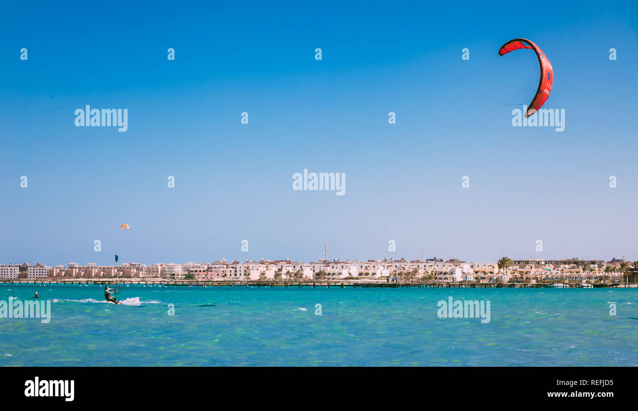 L'Egypte, Hurghada - 30 novembre, 2017 : Le kiteboarder de glisser sur la surface de la mer Rouge. Le cerf-volant rouge planeur dans le ciel bleu clair. Hurghada hôtels bac Banque D'Images