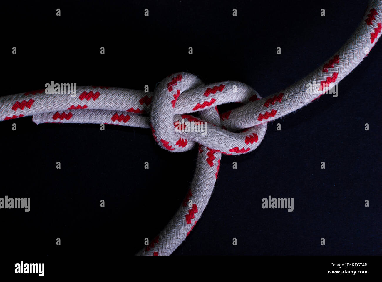 Close up d'un nœud dans une corde de voile rouge et blanc sur fond noir Banque D'Images