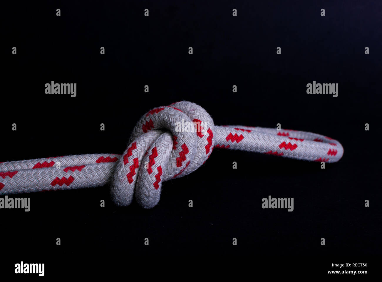 Close up d'un nœud dans une corde de voile rouge et blanc sur fond noir Banque D'Images