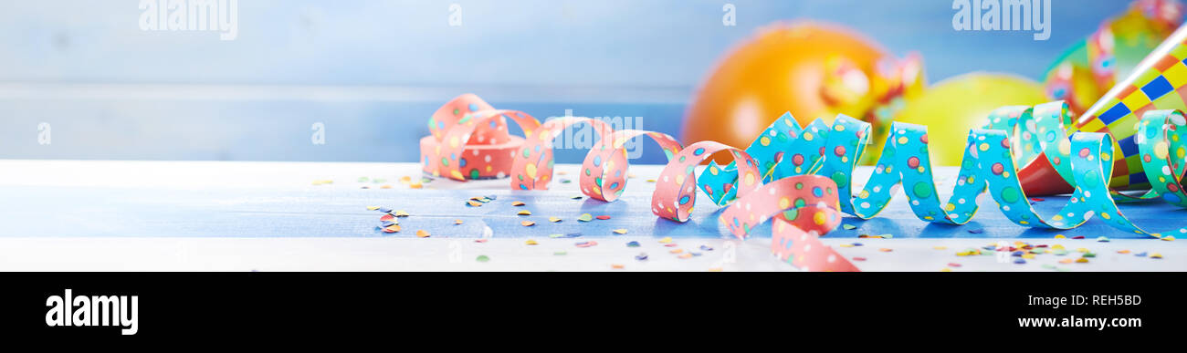 Fête de célébration bannière avec des ballons colorés, Serpentins et confettis éparpillés sur une surface en bois blanc avec copie espace dans un angle large pano Banque D'Images